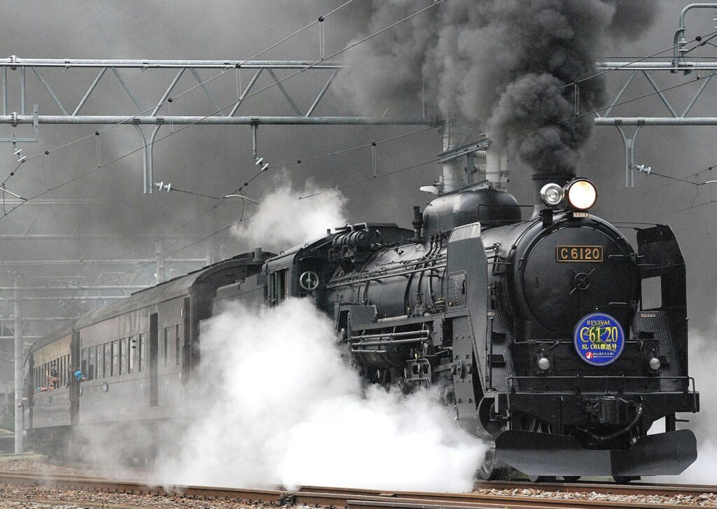 Steam locomotive releasing smoke and steam on a rail track, showcasing vintage train transportation.